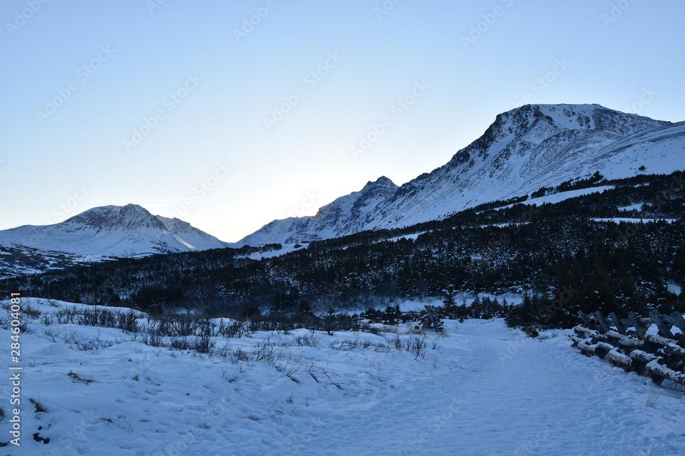 winter alpine meadow with sunrise and mountains in the background