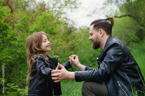 Modern stylish family walking in the park. Cute little daughter is calling dad to play. Time together. Family look. Urban casual outfit. Fatherhood makes life more livable photo