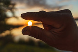 hands holding the sun at dawn. hand framing view distant over sunset