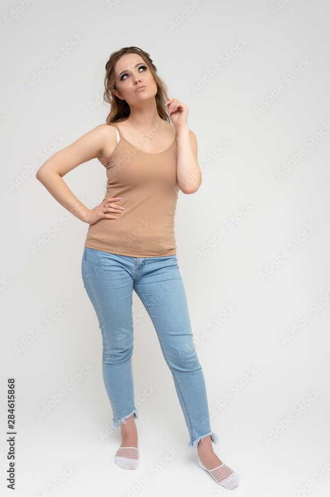 Photo full-length portrait of a pretty brunette woman girl with long beautiful curly hair on a white background in a t-shirt and blue jeans. Talking while standing in front of the camera. Photo full-length portrait of a pretty brunette woman girl with long beautiful curly hair on a white background in a t-shirt and blue jeans. Talking while standing in front of the camera.