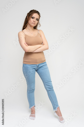 Photo full-length portrait of a pretty brunette woman girl with long beautiful curly hair on a white background in a t-shirt and blue jeans. Talking while standing in front of the camera.
