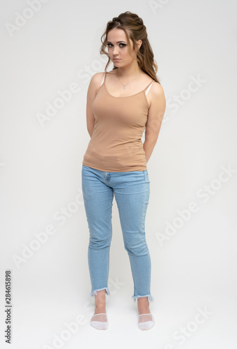 Photo full-length portrait of a pretty brunette woman girl with long beautiful curly hair on a white background in a t-shirt and blue jeans. Talking while standing in front of the camera.