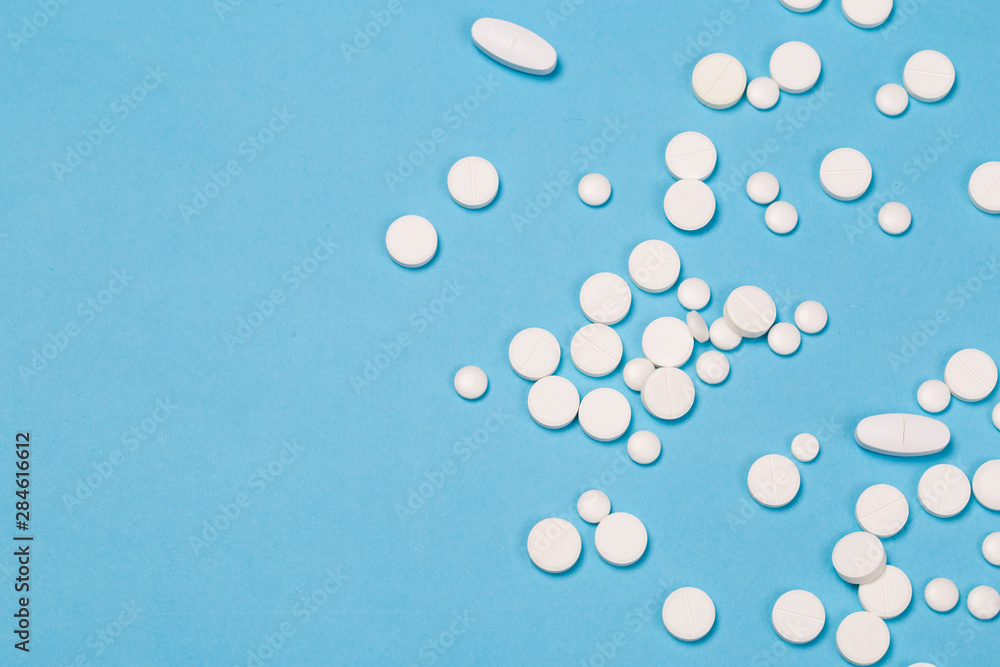 White Pills are scattered over a blue background. Close up. Medical background. White Pills are scattered over a blue background. Close up. Medical background.