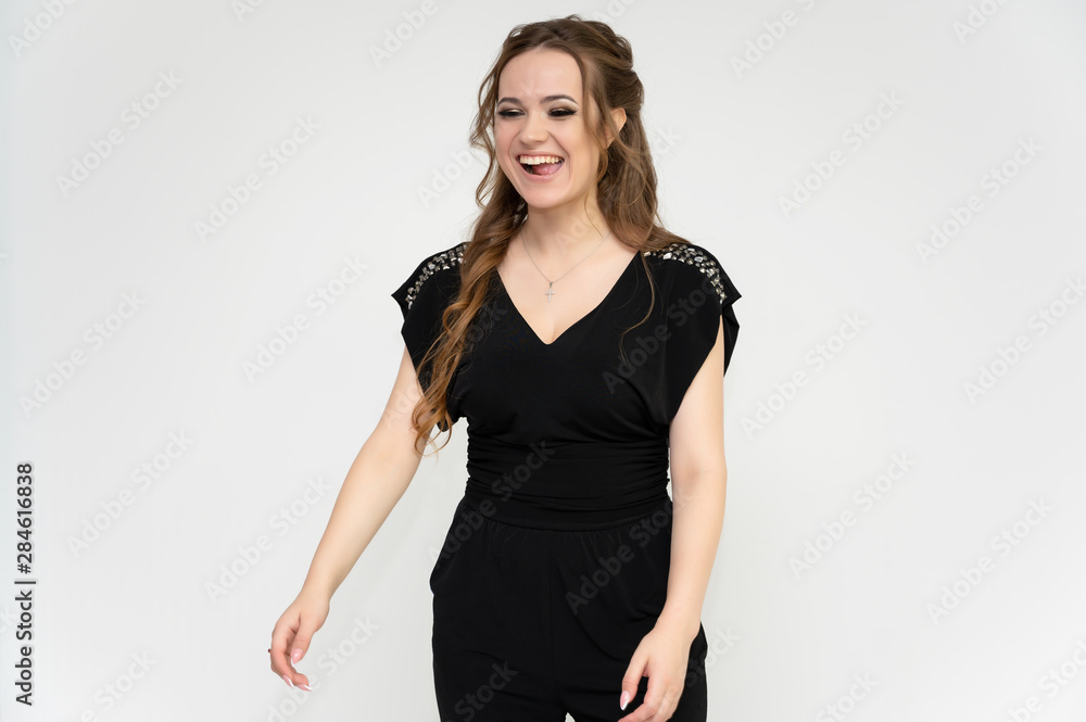 Photo portrait above the knee of a pretty girl of a brunette woman with long beautiful curly hair on a white background in a black dress. Talking while standing in front of the camera. Photo portrait above the knee of a pretty girl of a brunette woman with long beautiful curly hair on a white background in a black dress. Talking while standing in front of the camera.
