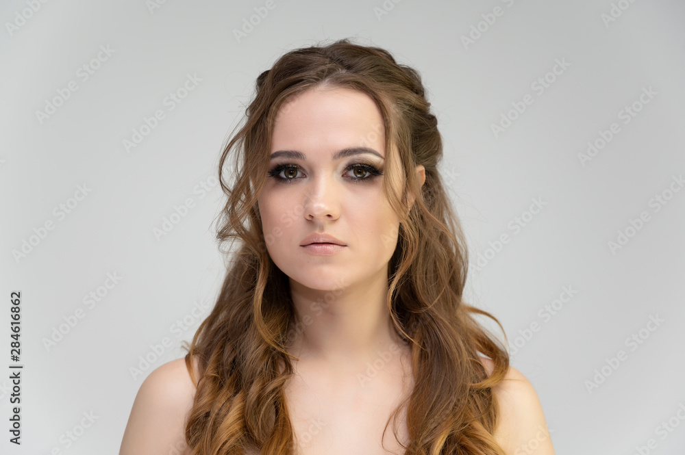 Naklejka premium Close-up photo portrait of a pretty brunette woman girl with long beautiful curly hair on a white background. Standing in front of the camera