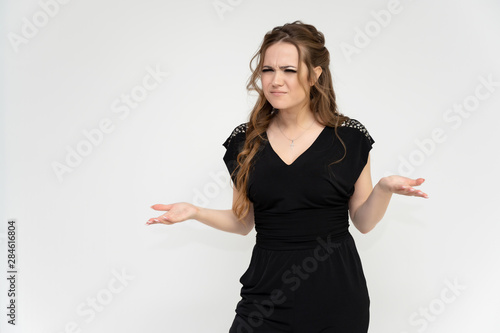 Photo portrait above the knee of a pretty girl of a brunette woman with long beautiful curly hair on a white background in a black dress. Talking while standing in front of the camera.