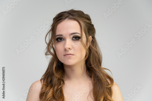 Close-up photo portrait of a pretty brunette woman girl with long beautiful curly hair on a white background. Standing in front of the camera