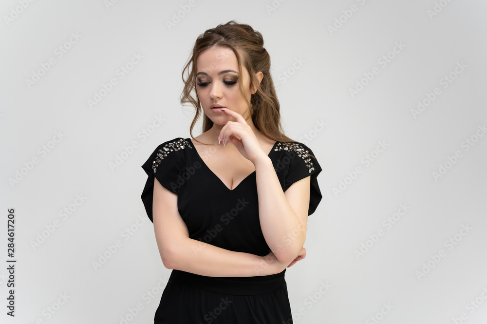 Fototapeta premium Photo waist-length portrait of a pretty brunette woman girl with long beautiful curly hair on a white background in a black dress. Talking in different poses. Standing facing the camera.