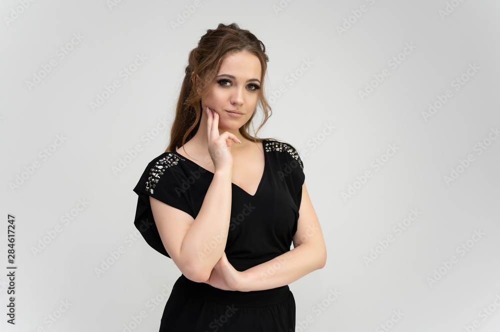 Photo waist-length portrait of a pretty brunette woman girl with long beautiful curly hair on a white background in a black dress. Talking in different poses. Standing facing the camera. Photo waist-length portrait of a pretty brunette woman girl with long beautiful curly hair on a white background in a black dress. Talking in different poses. Standing facing the camera.