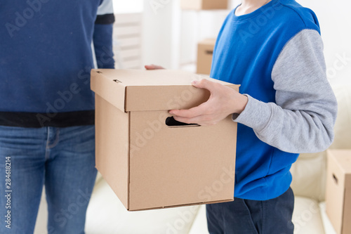 Close-up of teen boy holds a box and a pot of plants while moving to a new apartment. Housewarming and new housing concept. © satura_