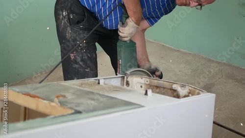 A man cuts a machine tool for metal, cuts a refrigerator, works for metal, an elderly man. experience with metal. A man in ordinary clothes with angle grinders while working in a metal cutting worksho photo