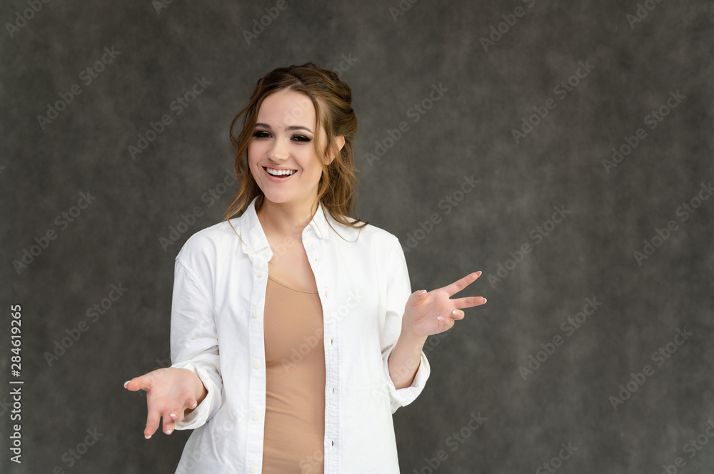 Photo waist-length portrait of a pretty brunette woman girl with long beautiful curly hair on a gray background in a white shirt. Talking in different poses. Standing facing the camera. Photo waist-length portrait of a pretty brunette woman girl with long beautiful curly hair on a gray background in a white shirt. Talking in different poses. Standing facing the camera.