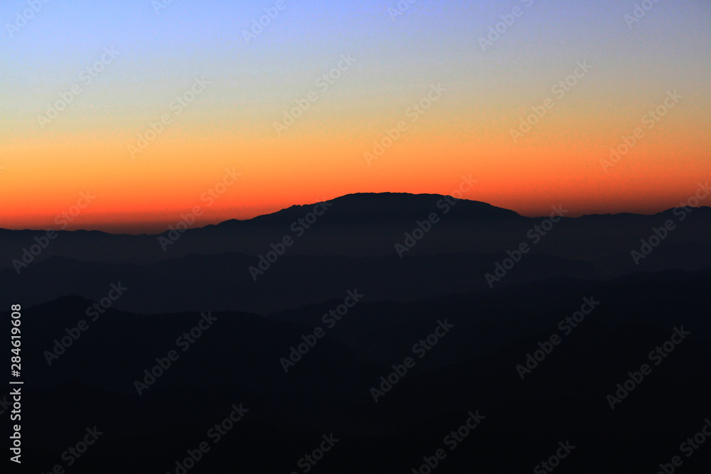 Sunset in sky and cloud, beautiful colorful twilight time with silhouette of mountain.