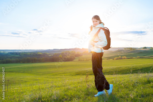 Tourist woman walking on a green hill trail with a backpack