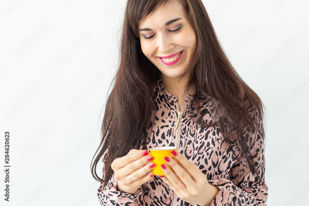 Playful young brunette woman holding in her hands a small yellow mug posing on a white background with copy space. Concept of morning coffee. Playful young brunette woman holding in her hands a small yellow mug posing on a white background with copy space. Concept of morning coffee.