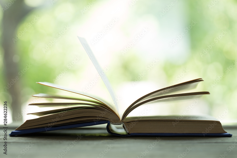 Open book on the wooden table, green summer background, education and reading concept Open book on the wooden table, green summer background, education and reading concept