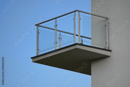 one balcony with glass railing against the blue sky on Sunny day. bottom view, modern building design, Scandinavian style with white walls
