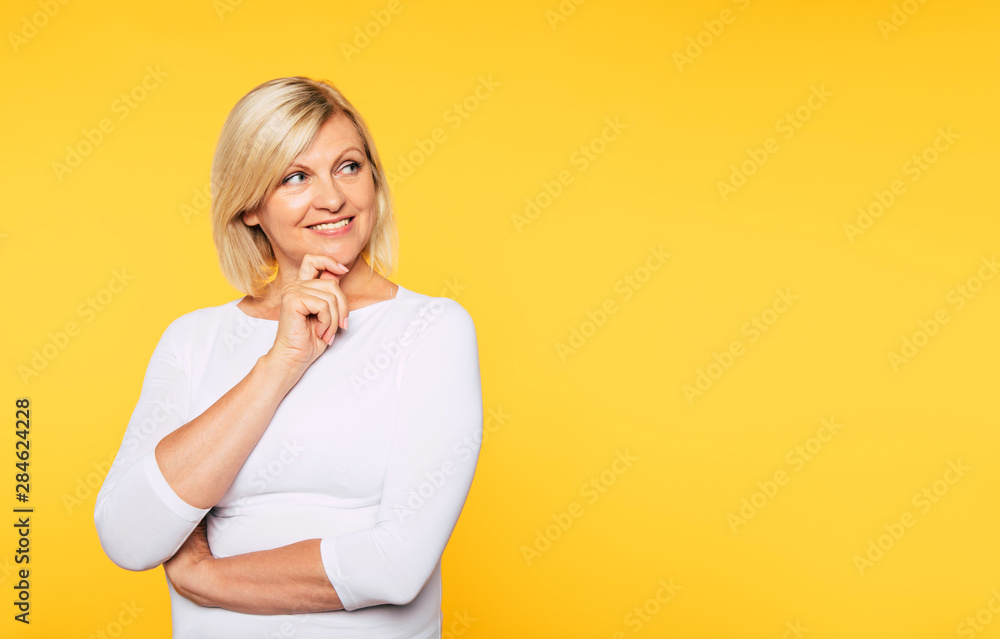 Happy smiling beautiful cute lovely blonde senior woman with beauty clean skin in casual wear isolated on yellow background. Healthcare and cosmetology concepts. Pensioner and mature people - obrazy, fototapety, plakaty 