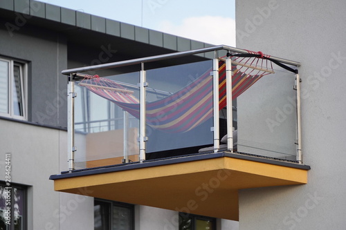 one balcony with glass railing and hammock against blue sky on a Sunny day. bottom view, Scandinavian style with white walls. rest in city