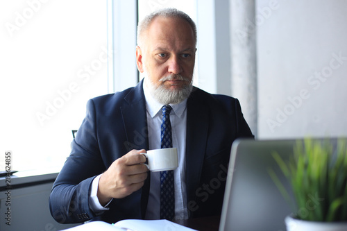 Mature businessman working on computer and drinking coffee in modern office.