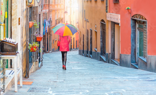 Fototapeta Naklejka Na Ścianę i Meble -  Woman in red clothes with multicolored umbrella - The high narrow house and Genoa is a historical port of city in northern italy