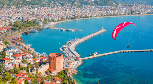 Fototapeta Naklejka Na Ścianę i Meble -  Paraglider tandem flying over marina and Red tower in Alanya peninsula, Antalya district, Turkey