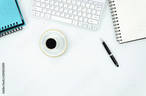 Keyboard and Notepad with pen and coffee cup on a white office desk. Freelance flat lay mockup