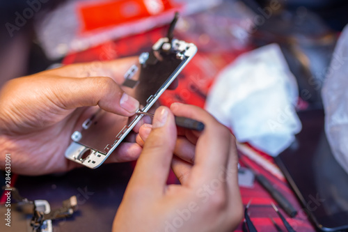 A man is repairing a mobile phone. In the frame  his hands and details of the device. repair shop for gadgets