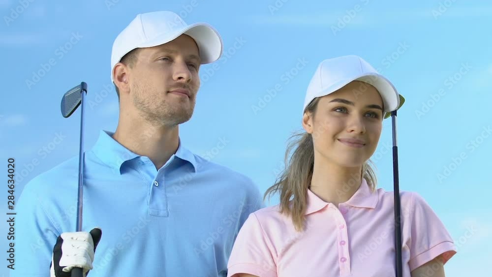 Inspired male and female golf players with clubs looking into distance at course Inspired male and female golf players with clubs looking into distance at course
