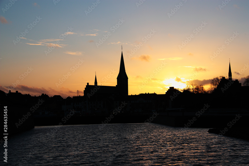 Sunset in an old European city (town) on a river. Dark silhouette of towers and buildings. Denmark