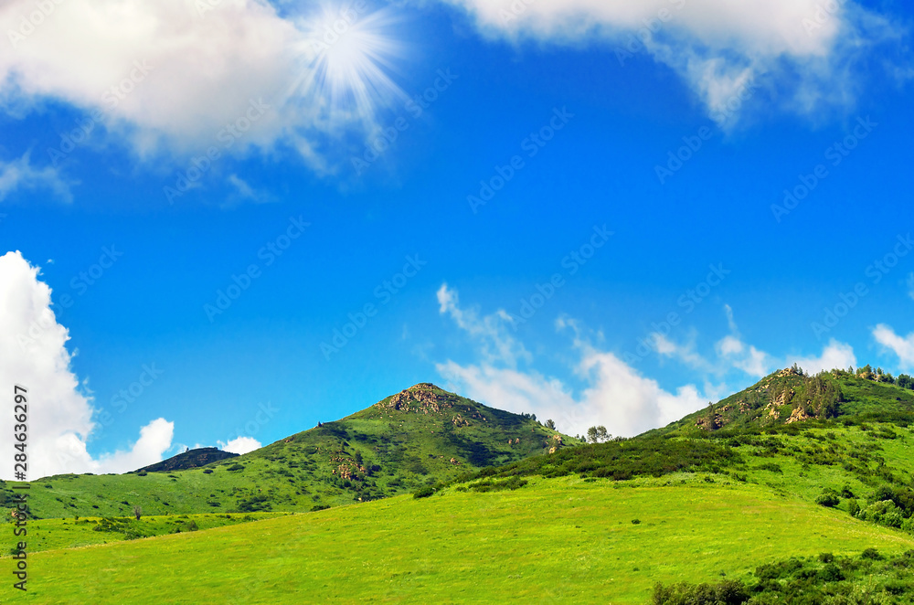 Summer Day with Blue Sky, White Clouds, Sunbeams over Green Mountains with Outcrops.