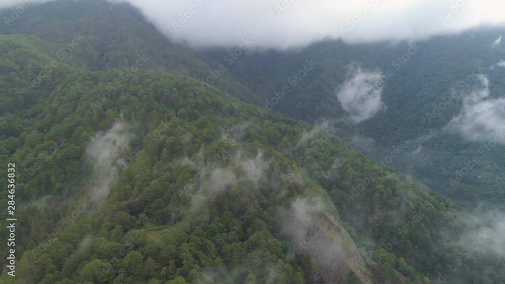 Aerial view mountains covered forest, trees in clouds and fog. Cordillera region. Luzon, Philippines. Slopes of mountains with evergreen vegetation. Mountainous tropical landscape. Aerial view mountains covered forest, trees in clouds and fog. Cordillera region. Luzon, Philippines. Slopes of mountains with evergreen vegetation. Mountainous tropical landscape.