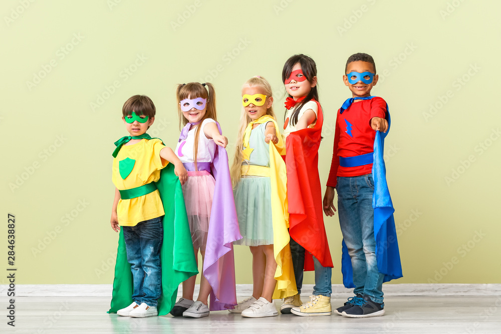 Naklejka premium Cute little children dressed as superheroes near color wall