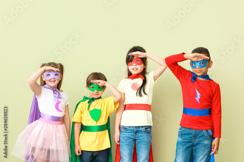 Cute little children dressed as superheroes on color background