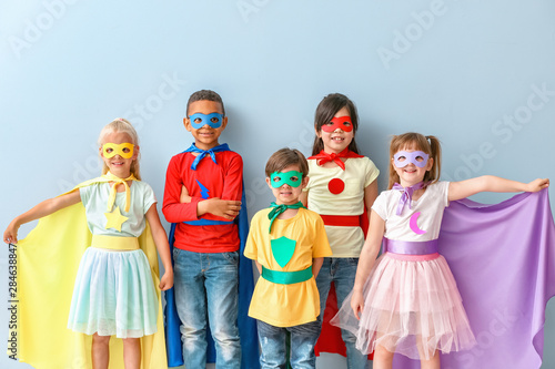 Cute little children dressed as superheroes on color background