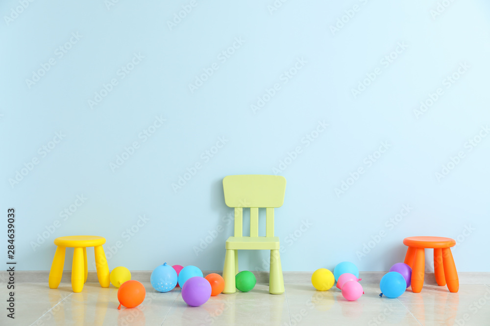 Chair, stools and balloons near color wall in children's room - obrazy, fototapety, plakaty 