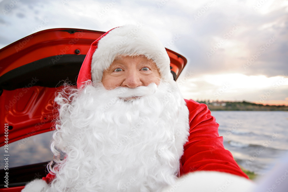 Obraz premium Santa Claus taking selfie near car on riverside