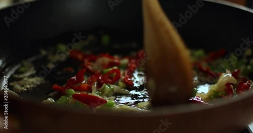 Wooden spoon stirring peppers, onions and herbs in a sizzling pan
