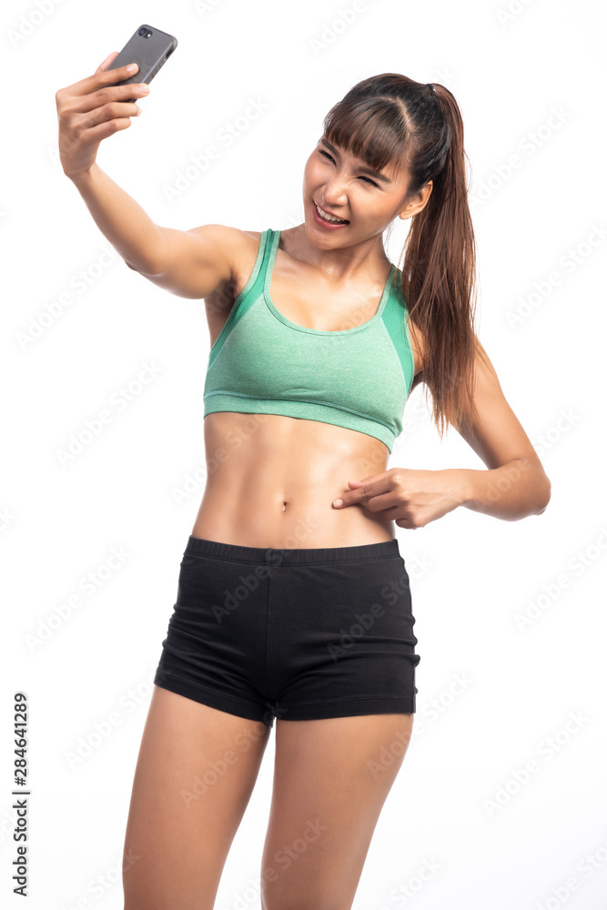 Fitness woman using mobile phone. Asia girl, doing selfie, pointing at her abs, happy smile. Fitness woman using mobile phone. Asia girl, doing selfie, pointing at her abs, happy smile.