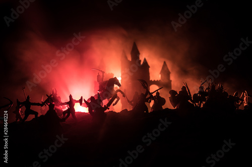 Medieval battle scene with cavalry and infantry. Silhouettes of figures as separate objects, fight between warriors on dark toned foggy background with medieval castle.