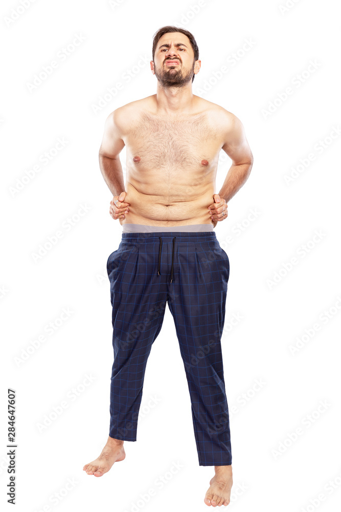 A young man is unhappy with fat on his stomach. Isolated over white background. Vertical.