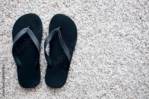 Pair of black rubber flip flops on white carpet