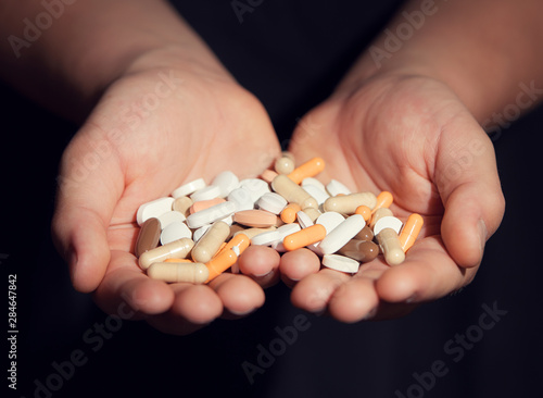 Kid holds stack of colorful pills and drugs in his palms on dark moody background. Concept of drug addiction and suicide.