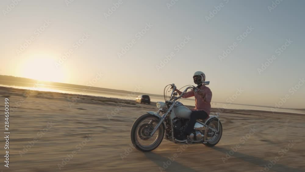 Young stylish motorcyclist driving his motorbike in the desert road during sunset Young stylish motorcyclist driving his motorbike in the desert road during sunset