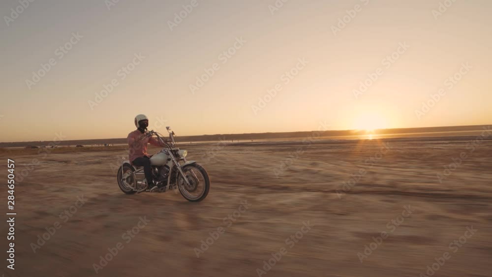 Young stylish motorcyclist driving his motorbike in the desert road during sunset Young stylish motorcyclist driving his motorbike in the desert road during sunset