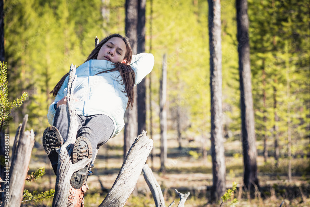 Sleepy girl in light jacket and boots sleeping on fallen tree after hike in the forest. Sleepy girl in light jacket and boots sleeping on fallen tree after hike in the forest.