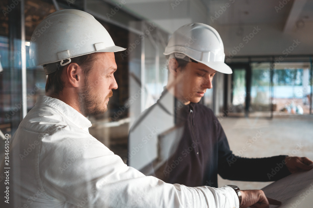 Worker and engineer have meeting while look drawing building under constuction. Two building engineers wearing safety hard hat discussing blueprint on construction site Worker and engineer have meeting while look drawing building under constuction. Two building engineers wearing safety hard hat discussing blueprint on construction site