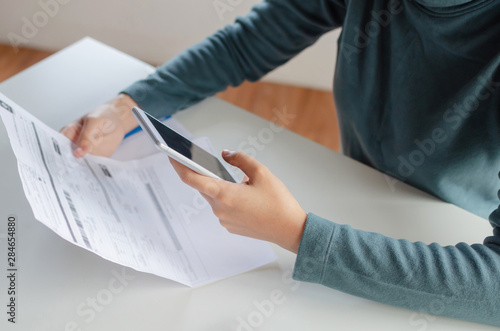 hands of young woman using mobile smart phone for scan and payment online with family budget cost bills on desk in home office, plan money cost saving, investment, business finance, expenses concept photo