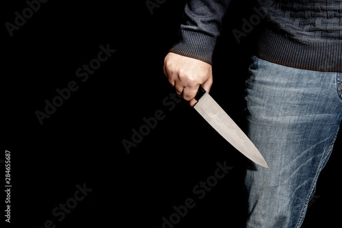 Man's hand holds a knife with copy space on black background. topics of violence and murder. thief, killer, rapist, maniac