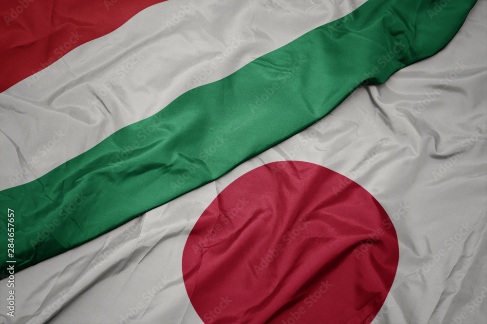 Obraz premium waving colorful flag of japan and national flag of hungary.